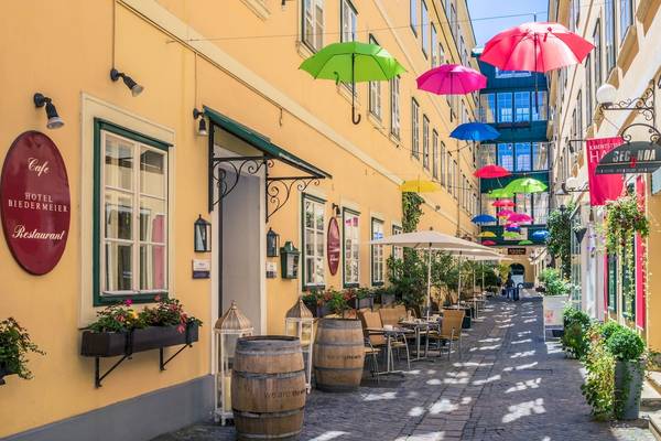 Außenbereich des Mercure Grand Hotel Biedermeier mit bunten Regenschirmen und bepflanzten Tischen.