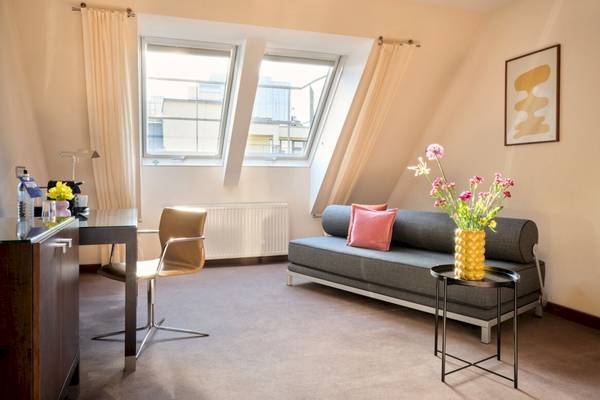 Zimmer im Flemings Hotel Wien-Stadthalle mit Schreibtisch, Stuhl, Couch, Tisch und Blumenvase.