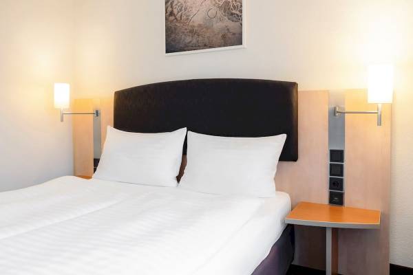 Doppelbett im Zimmer des IntercityHotel Wien mit weißen Laken und Kissen.