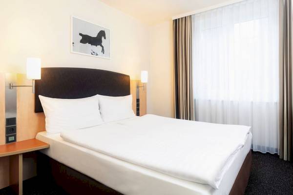 Ein Schlafzimmer im IntercityHotel Wien mit einem Bett, Kopfteil, weißen Kissen, und Wanddekoration.