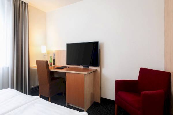 Innenansicht eines Zimmers im IntercityHotel Wien mit Schreibtisch, Fernseher und Stühlen.