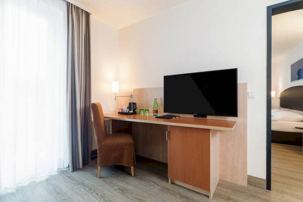 IntercityHotel Wien Zimmer mit Schreibtisch, Fernseher und Stuhl.