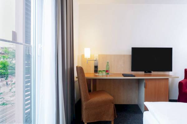Innenansicht eines Zimmers im IntercityHotel Wien mit Schreibtisch, Fernseher und Fenster.