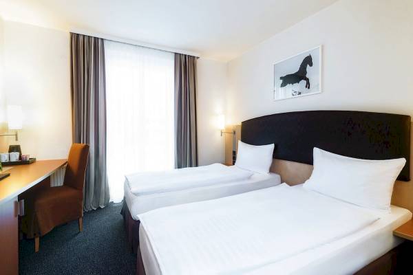 Doppelzimmer im IntercityHotel Wien mit zwei Betten, Schreibtisch und Stuhl.
