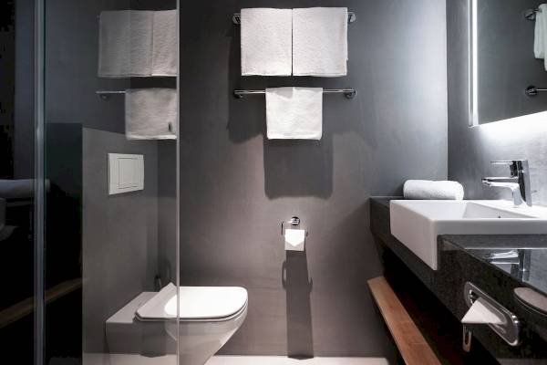 Badezimmer im IntercityHotel Wien mit grauen Wänden, weißen Handtüchern und modernem Design.