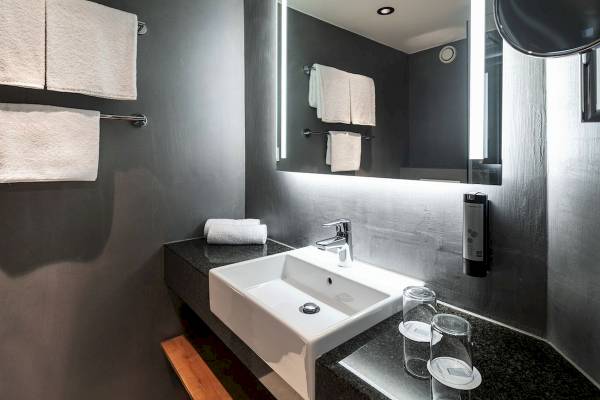 Badezimmer im IntercityHotel Wien mit Waschbecken, Spiegel und Handtüchern.