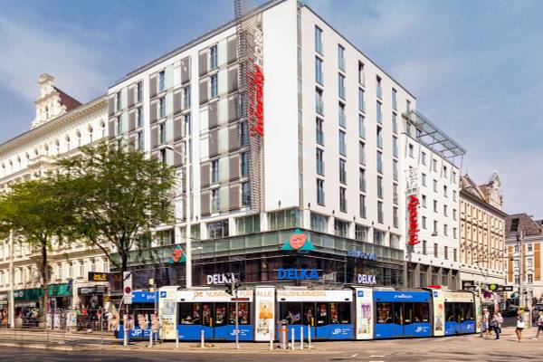 IntercityHotel Wien Hauptbahnhof an einer Stadtstraße mit Straßenbahnen und Passanten.