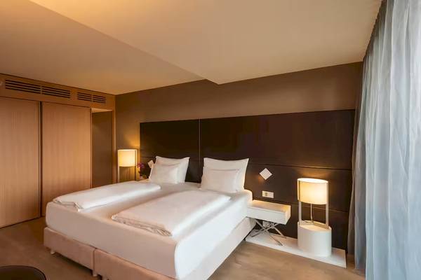 Doppelbett im Zimmer im DoubleTree by Hilton Vienna Schonbrunn mit weißen Laken und Kissen, zwei Nachttischen und Lampen.