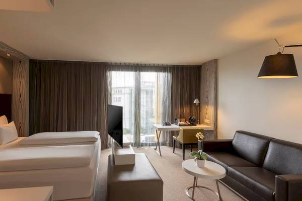 Doppelzimmer im DoubleTree by Hilton Wien Schonbrunn mit zwei Betten, Sofa, Schreibtisch und Fernseher.
