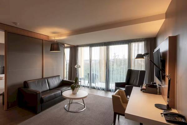 Innenansicht eines Hotelzimmers im DoubleTree by Hilton Vienna Schonbrunn mit einem Doppelbett, einer Couch, einem Tisch und einem Fernseher.