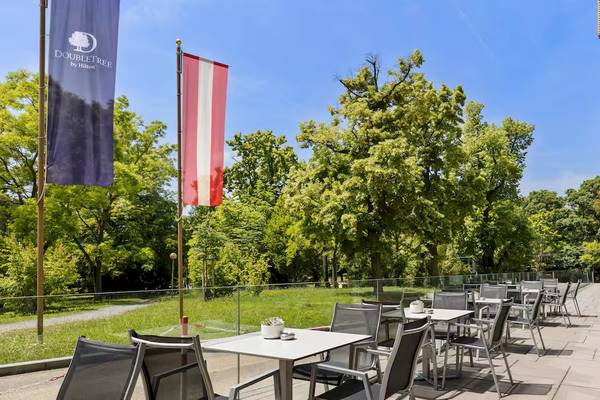 Terrasse des DoubleTree by Hilton Vienna Schonbrunn mit Tischen und Stühlen.