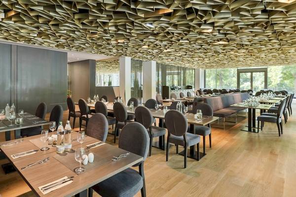 Innenraum des DoubleTree by Hilton Vienna Schonbrunn mit geometrischen Deckenelementen und gedeckten Tischplätzen.