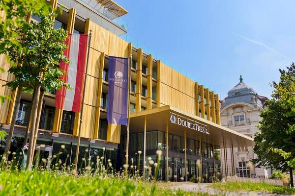 Außenansicht des DoubleTree by Hilton Vienna Schonbrunn mit gelben Fassaden und Bäumen vor dem Gebäude.