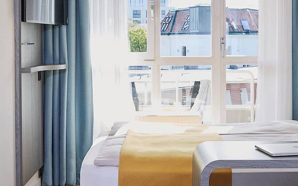 Ein modernes Hotelzimmer mit Blick auf die Stadt, einem Bett, Laptop und Blumen.