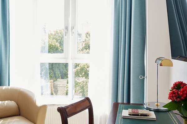 Hotelzimmer mit Fenster und Schreibtisch, einem Stuhl, einer Lampe und Blumen.