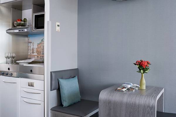 Eine Küchenecke im Living Hotel Kaiser Franz Joseph mit grauen Wänden, einer grauen Sitzbank, einem Tisch mit einer Vase mit roten Blumen, einer Mikrowelle und einer Dunstabzugshaube.