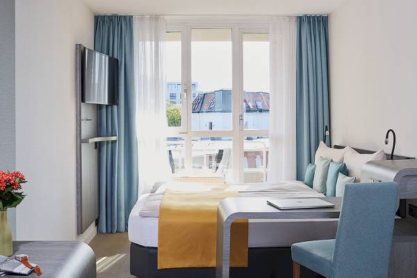 Hotelzimmer mit Bett, Schreibtisch, Stuhl und Sicht aus dem Fenster auf die Stadt.