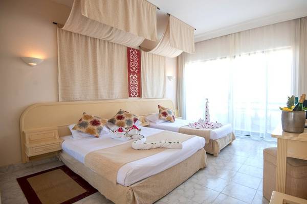 Doppelzimmer im Grand Hotel Hurghada mit zwei Betten, Dekor und einem Fenster mit Vorhängen.