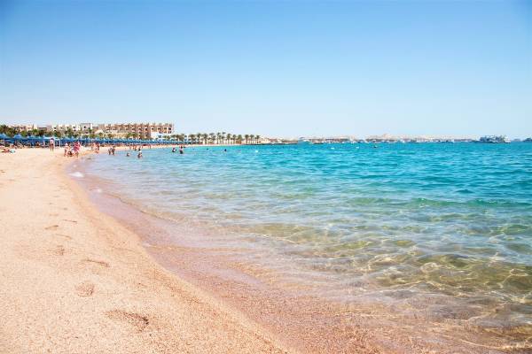 Strandansicht des Grand Hotel Hurghada mit blauem Wasser und mehreren Menschen.