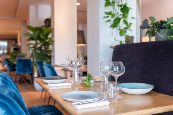 Inneneinrichtung des Restaurants im Crowne Plaza Paris République mit blauen Stühlen und runden Holztischen.
