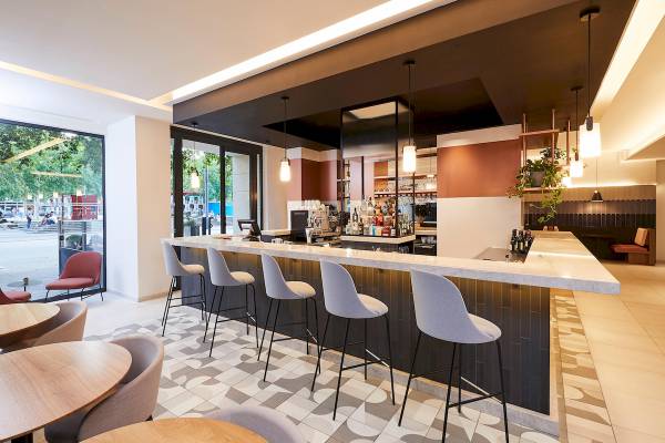 Bar im Crowne Plaza Paris République mit Barhockern, Theke und Pflanzen.