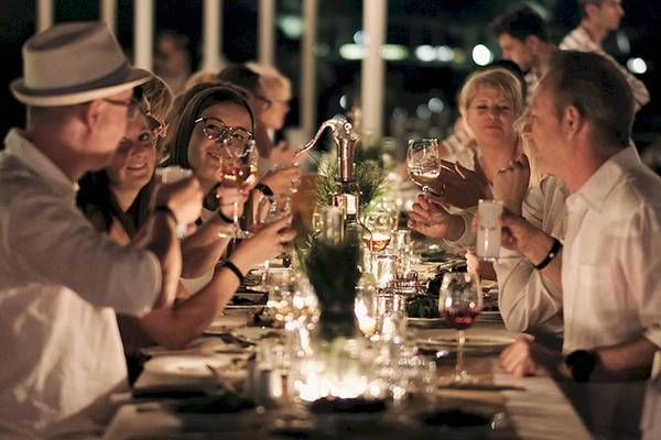 Gäste des Club Marvy sitzen bei einem Abendessen an einem langen Tisch, sie trinken und lachen.