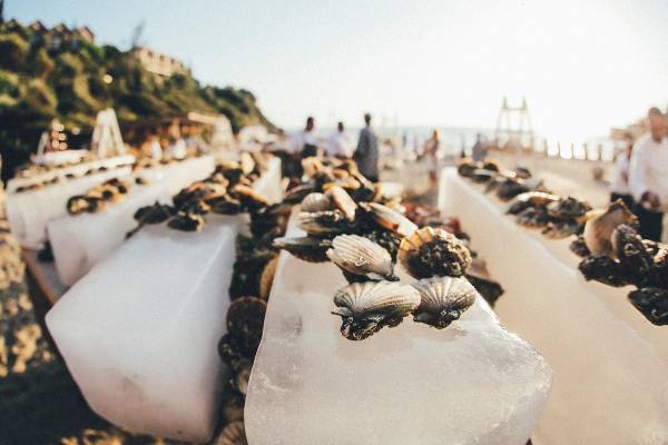 Ein Bild von Meeresfrüchten auf Eisblöcken, die am Strand von Club Marvy angeordnet sind, mit einigen Leuten im Hintergrund.