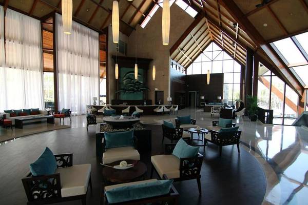 Lobby des JA Beach Hotel mit modernen Möbeln, hohen Decken und großen Fenstern.