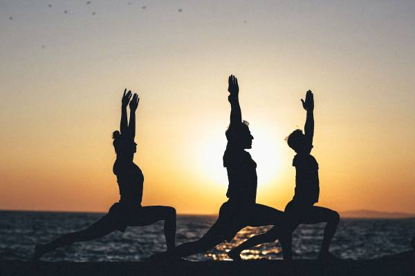 Drei Menschen in Yoga-Posen am Strand bei Sonnenuntergang.