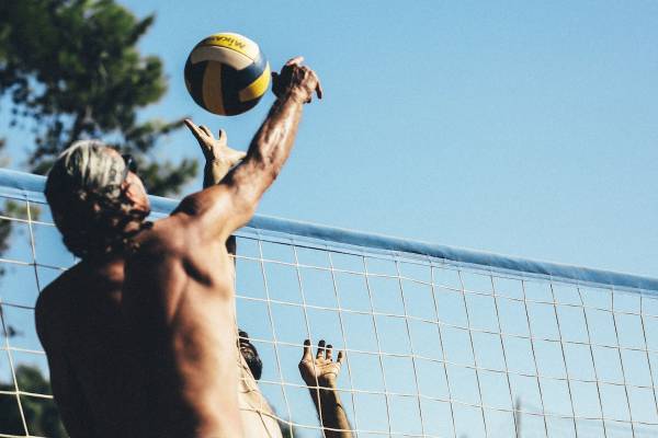 Zwei Männer spielen Volleyball vor einem Netz an einem sonnigen Tag.