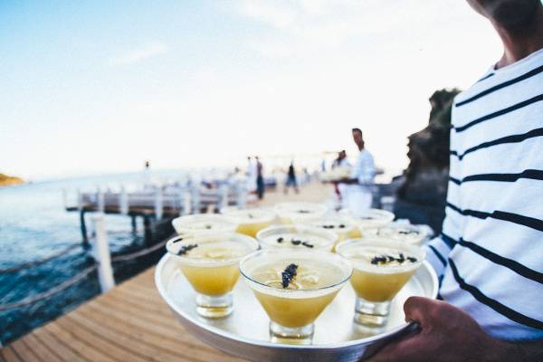 Cocktails auf einem Tablett am Strand, vor einem Hotel im Hintergrund.