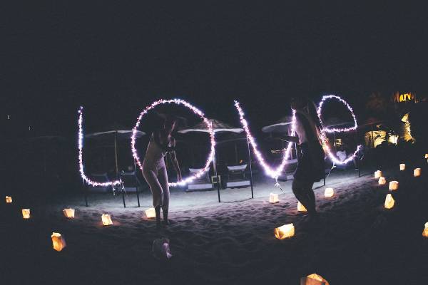 Zwei Personen tanzen mit Lichterketten in der Nacht auf dem Strand vor dem Club Marvy.