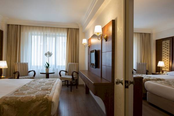 Innenansicht eines Hotelzimmers von Yigitalp Hotel mit zwei Betten, Sesseln und Fernseher.