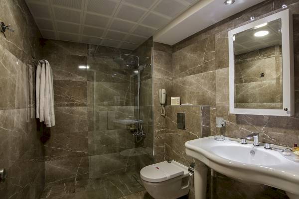 Innenansicht des Badezimmers im Yigitalp Hotel mit marmorierten Wänden, Glasdusche, Toilette und Waschbecken.