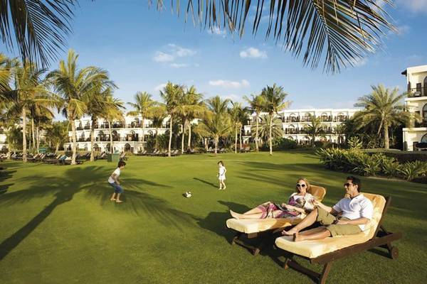 Familie im Lounge-Bereich des JA Beach Hotel mit Kindern, die auf dem Rasen spielen.
