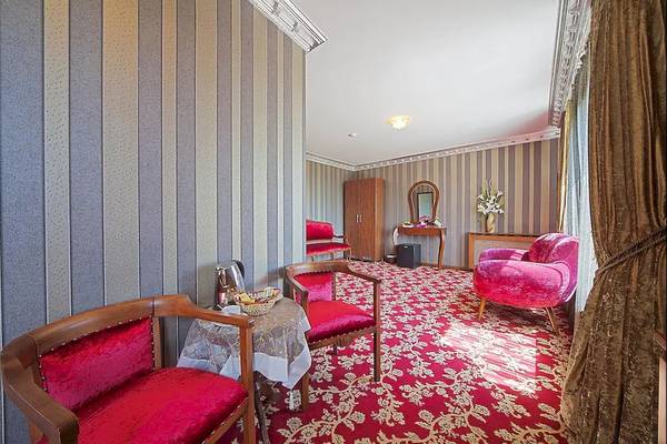 Innenansicht eines Zimmers im Antea Palace Hotel & Spa mit rotem Teppich, roten Sesseln und einem Tisch.