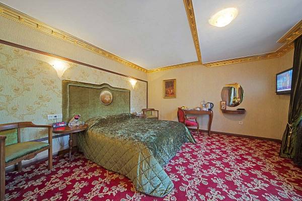 Ein elegantes Hotelzimmer mit einem großen Bett, grünen Kopfteilen, einem Tisch und Stühlen.