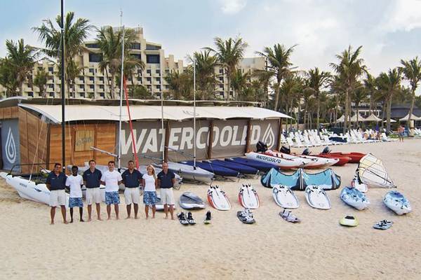 Ein Team von Wassersportlern steht vor dem Wassersportpavillon des JA Beach Hotels.