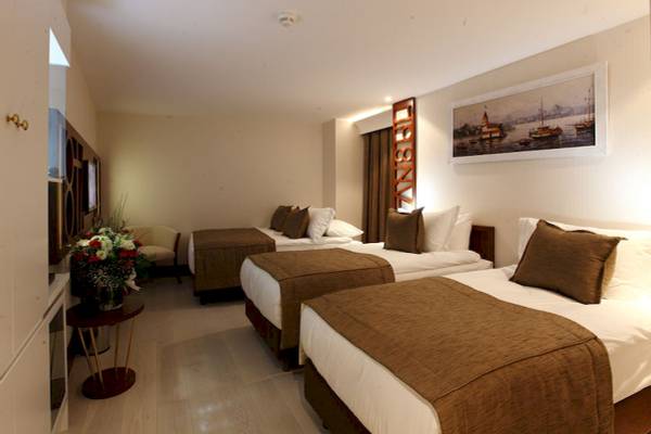 Innenansicht eines Doppelzimmers im Victory Hotel & Spa Istanbul mit drei Betten, einem Tisch mit Blumen und einem Gemälde an der Wand.