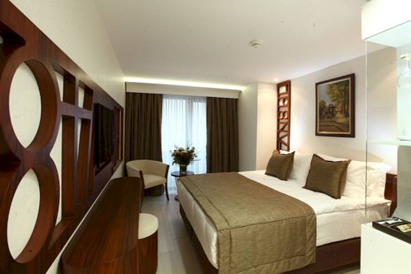 Schlafzimmer im Victory Hotel & Spa Istanbul mit großem Bett, braunen Kissen und Blumenvase auf Nachttisch.