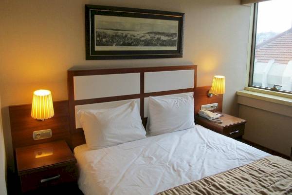 Hotelzimmer mit Bett, weißen Kissen, Nachttischen und Wandbeleuchtung.