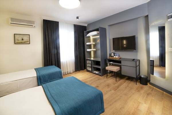 Innenansicht eines Hotelzimmers im Barin Hotel mit zwei Betten, einem Fernseher und einem Schreibtisch.