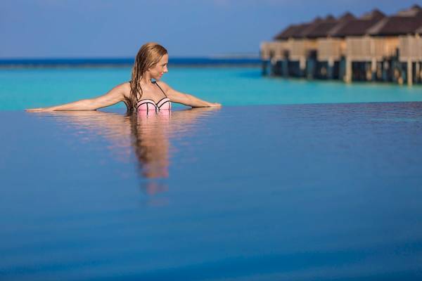 Frau im Schwimmbad von Sun Siyam Iru Fushi mit Blick auf Wasser und Überwasser-Bungalows