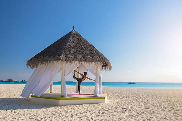 Eine Frau praktiziert Yoga in einem Pavillon am Strand des Sun Siyam Iru Fushi.
