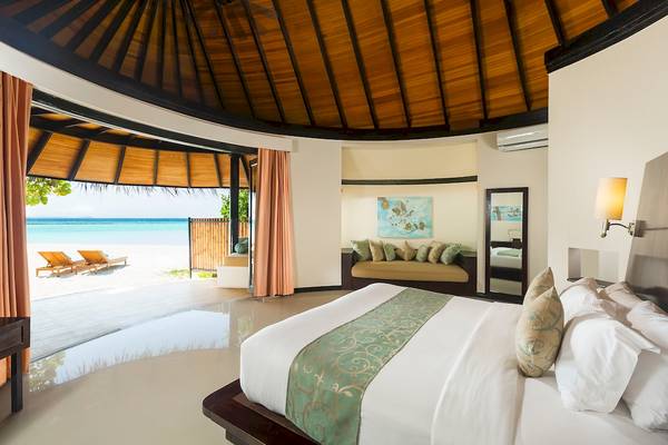 Schlafzimmer im Sun Siyam Iru Fushi Hotel mit Blick auf den Strand und zwei Sonnenliegen.