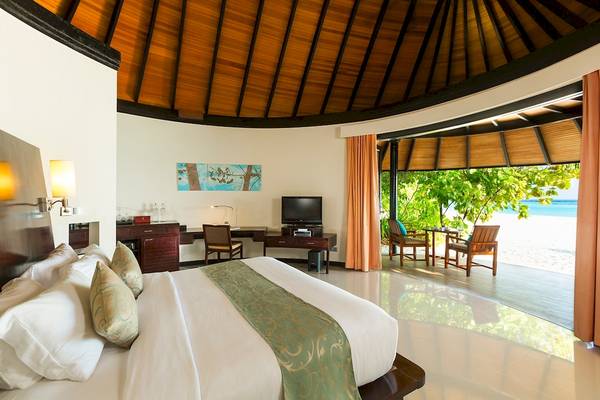 Schlafzimmer des Sun Siyam Iru Fushi Hotels mit großem Bett und Aussicht auf den Strand.