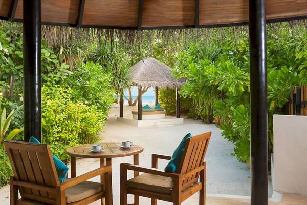 Terrasse mit Sitzen und Tisch im Sun Siyam Iru Fushi Hotel, Blick auf den Strand.