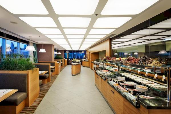 Innenansicht des Restaurants im Doubletree by Hilton Istanbul Moda Hotel mit modernen Möbeln, Pflanzen und einer langen Essenstheke.