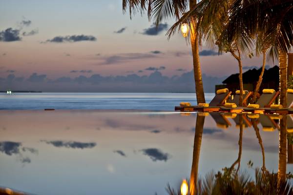 Ein Hotelpool mit Sonnenliegen und Palmen bei Sonnenuntergang am Meer