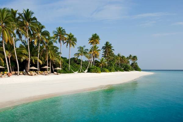 Sonnenuntergang am Strand des Sun Siyam Iru Fushi mit Palmen und Liegestühlen